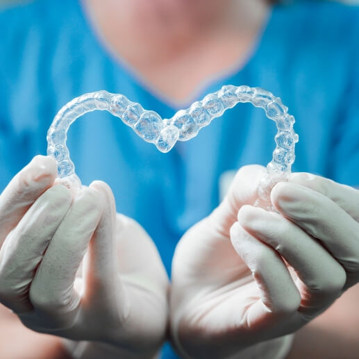 Dental team member holding two Invisalign aligners in the shape of a heart