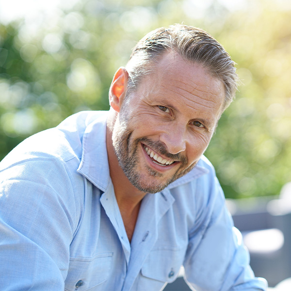 Man in button-up shirt smiling outside