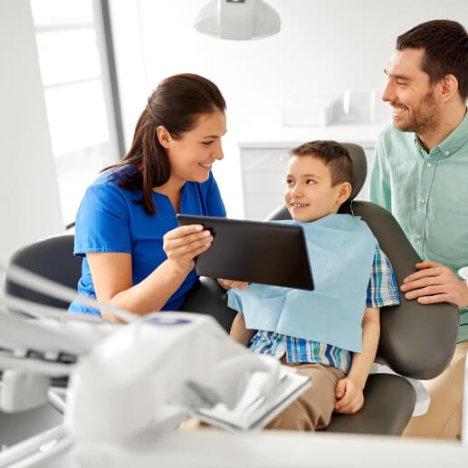 Dentist showing a tablet to a young boy in dental chair