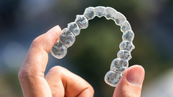 Hand holding an Invisalign clear aligner in Frisco
