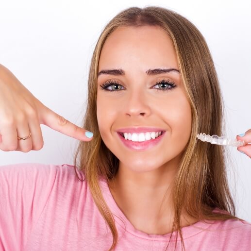 Woman holding Invisalign aligner and pointing to her smile