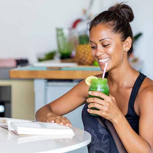 Smiling woman drinking green smoothie while reading